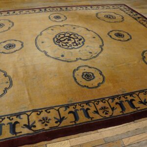 Mustard rug with navy blue floral medallions and a multi-layered border rests on light wood plank flooring.