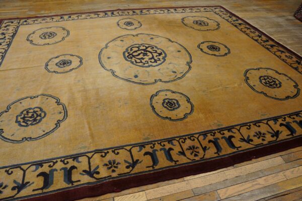 Mustard rug with navy blue floral medallions and a multi-layered border rests on light wood plank flooring.