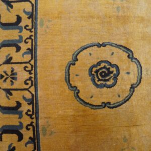 Close-up of a golden yellow rug with navy floral medallions and an intricate border on wood plank flooring.