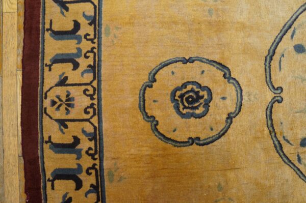 Close-up of a golden yellow rug with navy floral medallions and an intricate border on wood plank flooring.