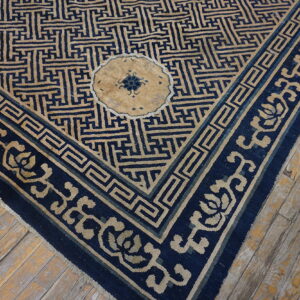 The corner of a tan and dark blue rug with geometric designs rests on heavily distressed wooden floorboards.