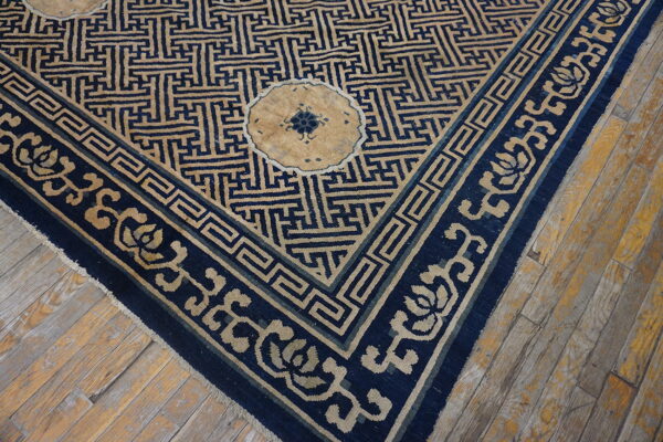 The corner of a tan and dark blue rug with geometric designs rests on heavily distressed wooden floorboards.