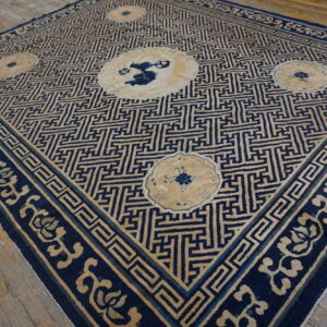 Blue and tan rug with a geometric maze pattern, floral borders, and medallions on wood flooring.