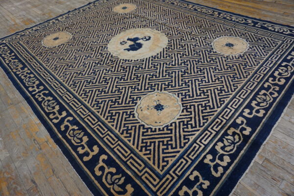 Blue and tan rug with a geometric maze pattern, floral borders, and medallions on wood flooring.