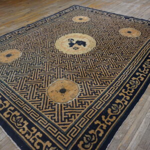 Rectangular low-pile rug featuring a blue and tan meander pattern with medallions on light wood flooring.