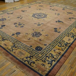 Muted pink rug with blue and gold floral patterns and geometric borders on hardwood floor.