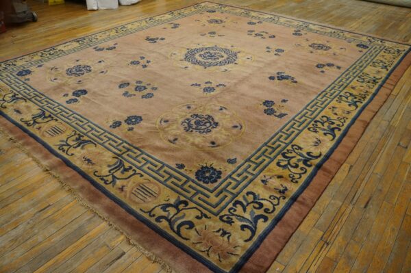 Muted pink rug with blue and gold floral patterns and geometric borders on hardwood floor.