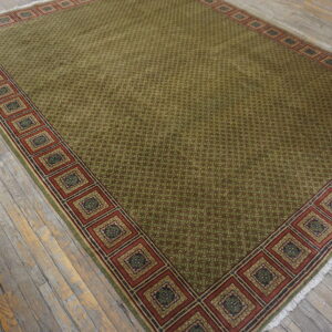 Green patterned rug featuring a wide, square-motif border resting on rustic, distressed wooden planks.