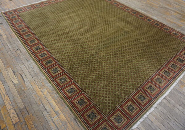 Green patterned rug featuring a wide, square-motif border resting on rustic, distressed wooden planks.