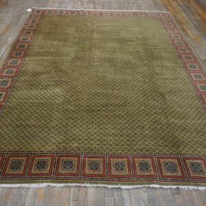 Olive green geometric rug featuring a wide border of repeating square medallions on distressed wooden flooring.