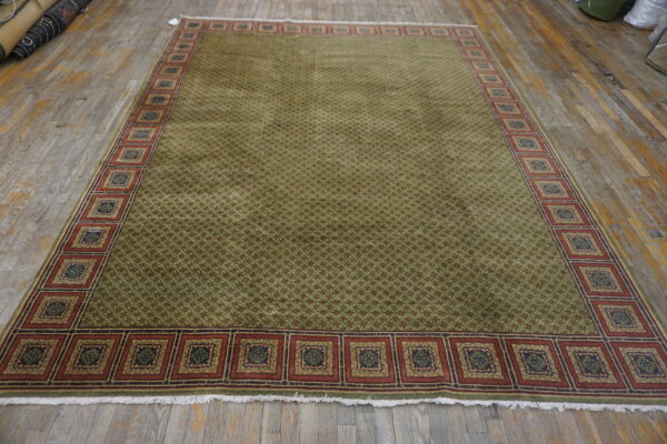 Olive green geometric rug featuring a wide border of repeating square medallions on distressed wooden flooring.
