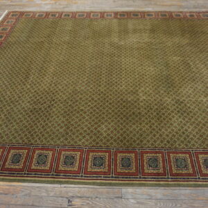 Green and red patterned rug with a wide square medallion border resting on distressed wood flooring.