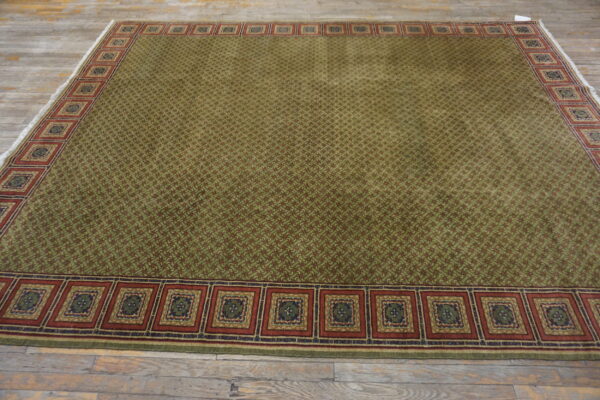 Green and red patterned rug with a wide square medallion border resting on distressed wood flooring.