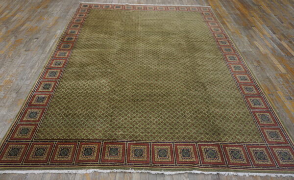 Olive green patterned rug featuring a red medallion border, displayed on distressed wood flooring.
