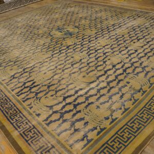 Gold and dark blue rug with repeating cloud motifs and geometric borders resting on wood plank flooring.