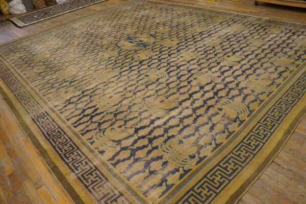 Gold and dark blue rug with repeating cloud motifs and geometric borders resting on wood plank flooring.
