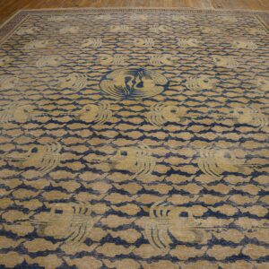 Tan and blue rug with stylized flying cranes and cloud pattern on wooden plank flooring.