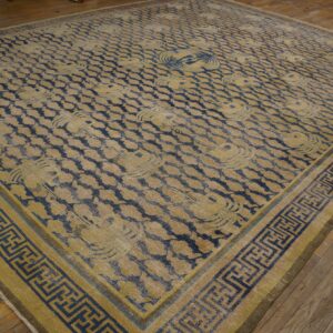 Large blue and faded yellow rug with repeating patterns and a geometric key border on wood floor.