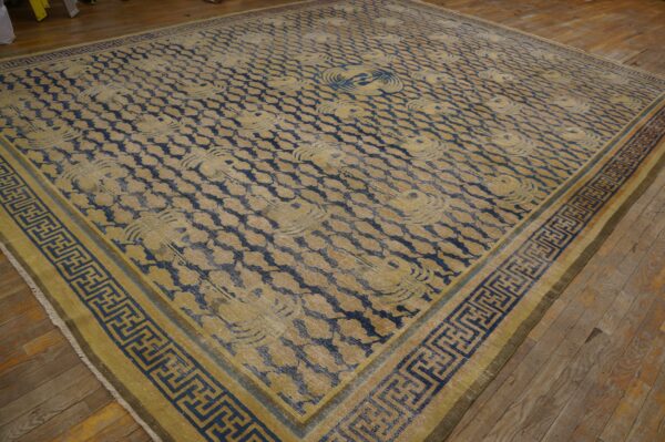 Large blue and faded yellow rug with repeating patterns and a geometric key border on wood floor.