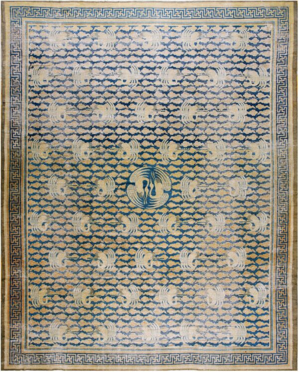 Worn blue and tan rug featuring repeating stylized bird patterns and a geometric greek key border.
