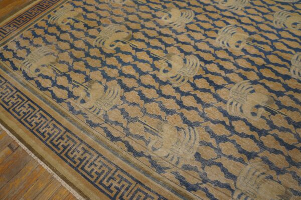 Distressed blue and gold rug with repeating crane patterns and a greek key border on wood flooring.