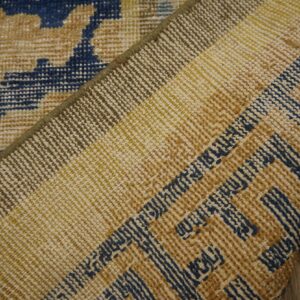 The rug's underside, featuring tan, yellow, and blue weaving, is folded over a blue and tan patterned face.