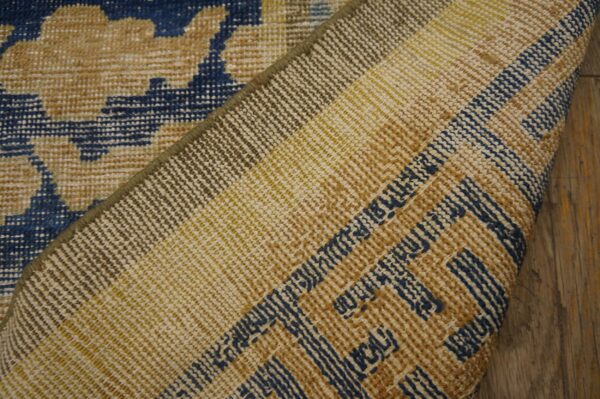 The rug's underside, featuring tan, yellow, and blue weaving, is folded over a blue and tan patterned face.