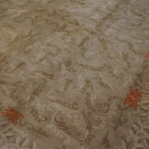 A high-pile beige rug features a tone-on-tone scrolling pattern and distinct orange floral motifs near the border.