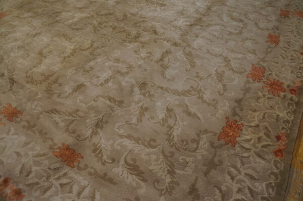 A high-pile beige rug features a tone-on-tone scrolling pattern and distinct orange floral motifs near the border.