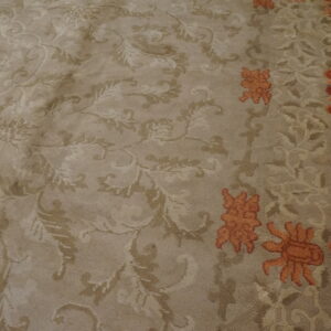 High-pile beige rug with tone-on-tone floral scrolls and rust accents borders distressed wood flooring.