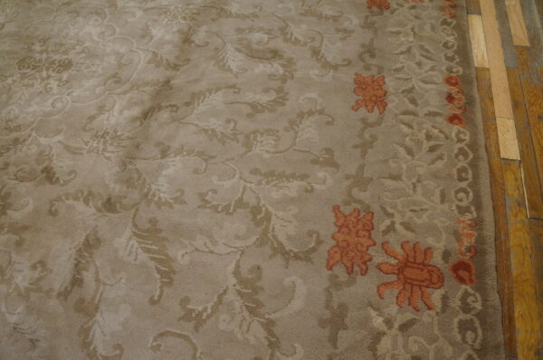 High-pile beige rug with tone-on-tone floral scrolls and rust accents borders distressed wood flooring.