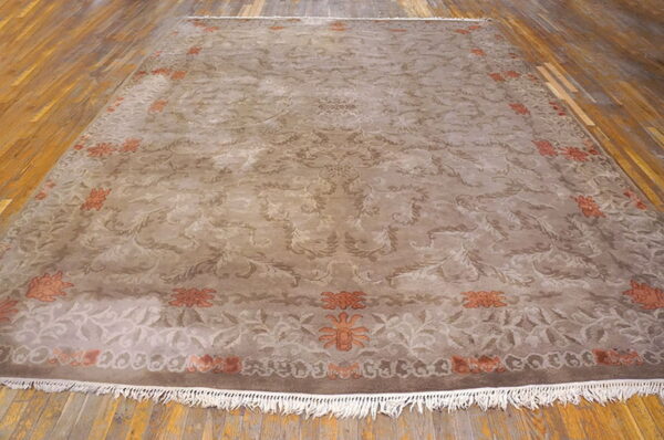 Traditional taupe rug with scrolling brown and rusty orange accents displayed on distressed hardwood flooring.