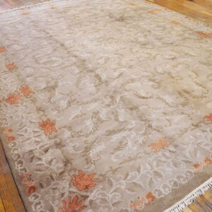 A large beige and taupe rug with scrolling traditional patterns and orange floral accents on wood floors.