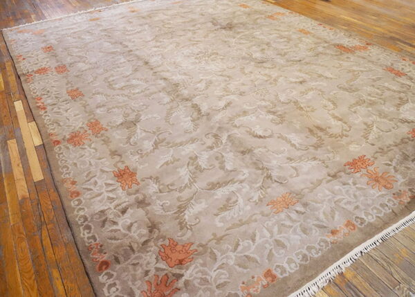 A large beige and taupe rug with scrolling traditional patterns and orange floral accents on wood floors.