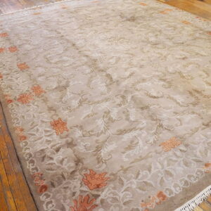 Ornate beige rug with cream floral patterns and orange border motifs rests on rustic wood flooring.