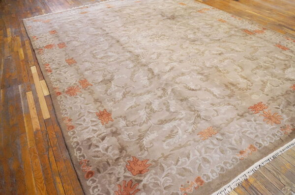 Ornate beige rug with cream floral patterns and orange border motifs rests on rustic wood flooring.