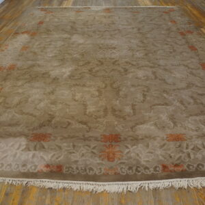 Taupe rug featuring tonal scrolling florals and orange border motifs rests on a warm wood floor.