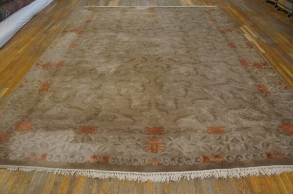 Taupe rug featuring tonal scrolling florals and orange border motifs rests on a warm wood floor.