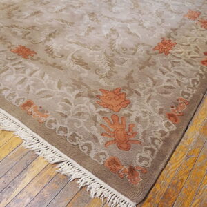Taupe and beige low-pile rug with rust floral accents and fringe rests on distressed wood flooring.