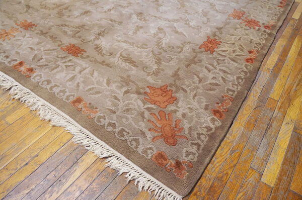 Taupe and beige low-pile rug with rust floral accents and fringe rests on distressed wood flooring.