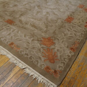 Beige-taupe rug with detailed scrolling floral patterns and rust-orange accents on distressed wood planks.