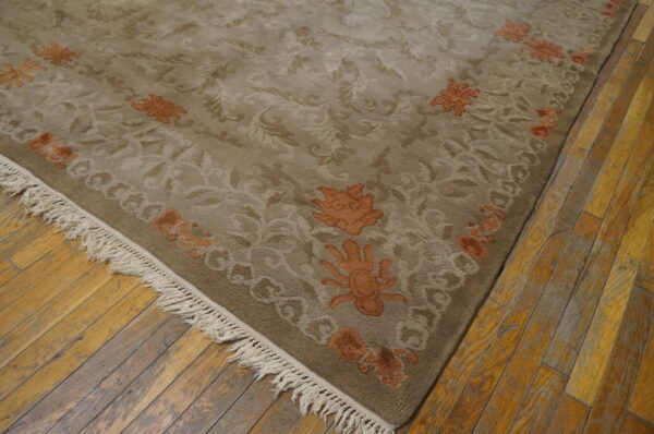 Beige-taupe rug with detailed scrolling floral patterns and rust-orange accents on distressed wood planks.