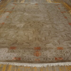 Taupe rug with tonal scrollwork and orange floral accents displayed on distressed wood flooring.