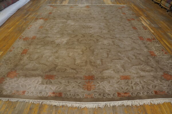 Taupe rug with tonal scrollwork and orange floral accents displayed on distressed wood flooring.