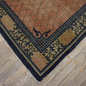 Low-pile rug corner in terracotta and navy/olive scroll patterns rests on light, distressed wood plank flooring.