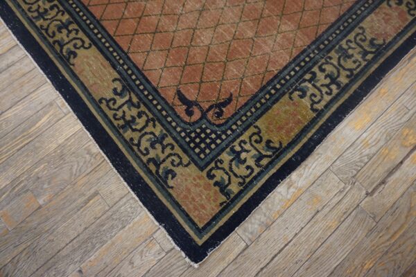 Low-pile rug corner in terracotta and navy/olive scroll patterns rests on light, distressed wood plank flooring.