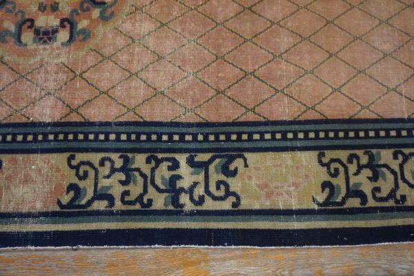 Close-up of a low-pile rug featuring a salmon diamond lattice field and multi-band border with navy scrollwork on wood flooring.