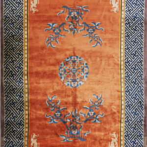 Orange rug with blue and light blue floral patterns and wide navy geometric fretwork borders.