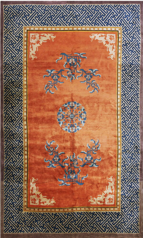 Orange rug with blue and light blue floral patterns and wide navy geometric fretwork borders.