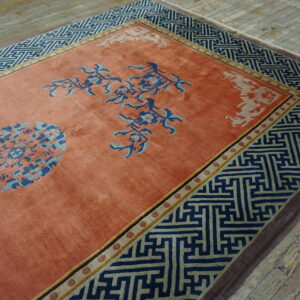 A salmon rug with navy Greek key borders and blue floral medallions rests on weathered wood floors.
